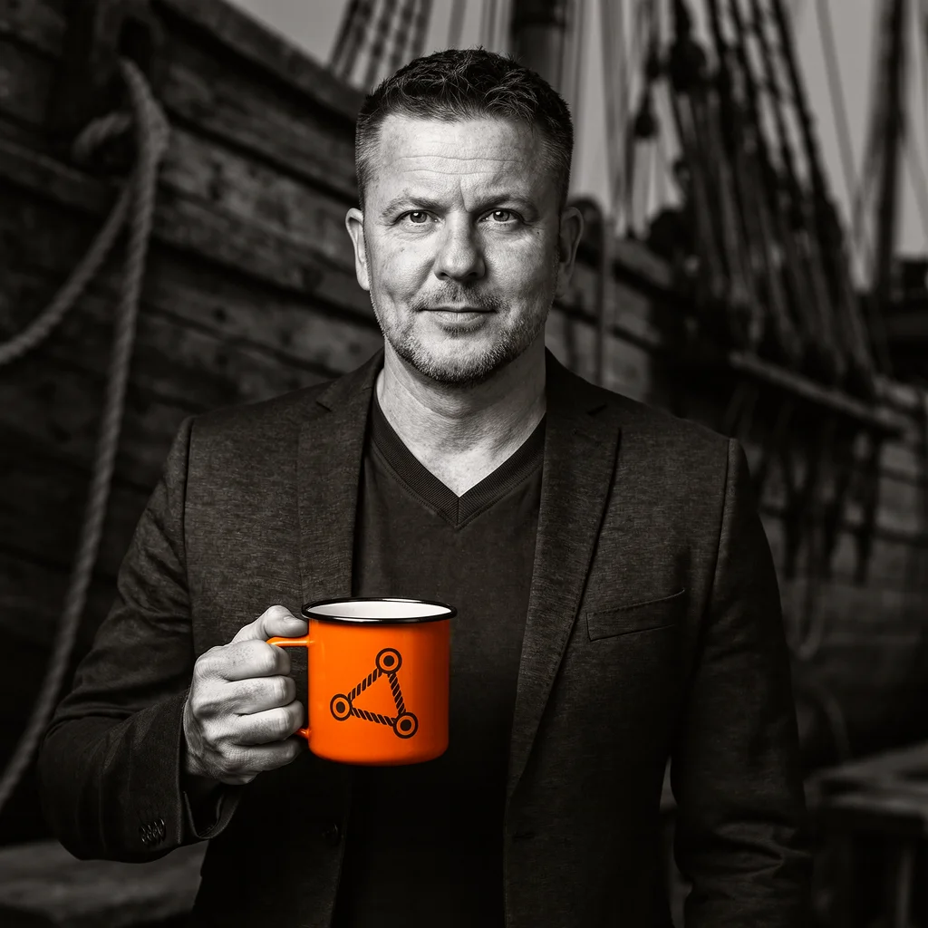 Schwarzweiß-Porträt von Marcus Jurkat im maritimen Umfeld, mit orangefarbenem Becher in der Hand.