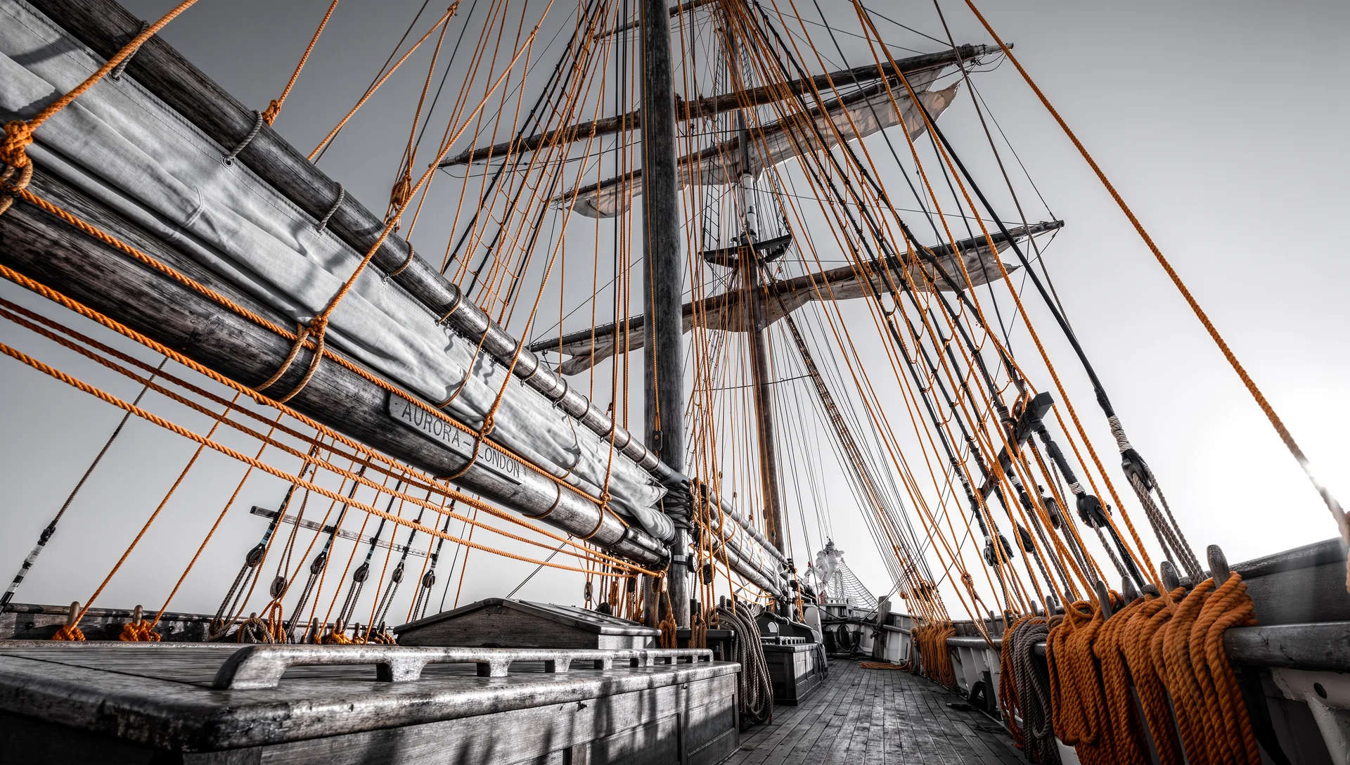 Takelage eines Segelschiffs in Schwarzweiß mit orangefarbenen Akzenten.