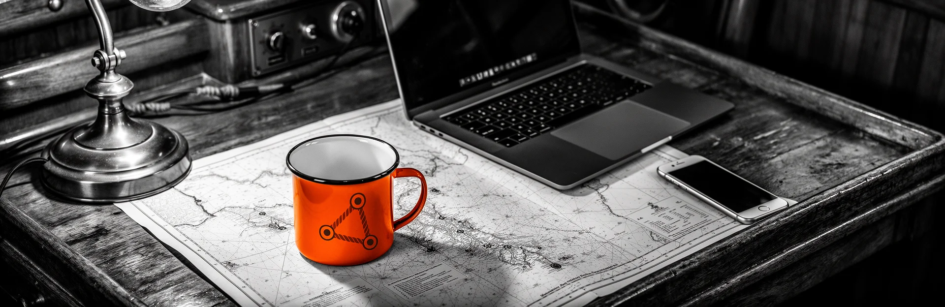 Kajüte mit Schreibtisch, Seekarten und digitalem Gerät in Schwarzweiß mit orangefarbenem Akzent.