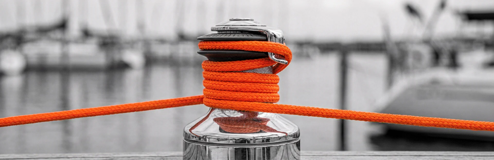 Detail einer Winsch mit orangefarbenem Tau in Schwarzweiß.